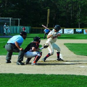 Harwich Mariners A baseball player at home plate ready to hit a ball. The umpire and catcher are behind him