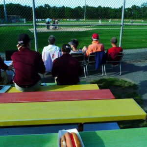 A group of people sitting on green, yellow and red bleachers watching a baseball game