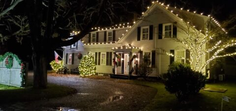 The exterior of a 1800s house at night with lights on the roofline all decorated for Christams