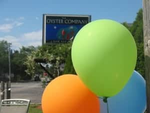 Three colorful balloons: lime green, orange and light blue in front of a restaurant sign