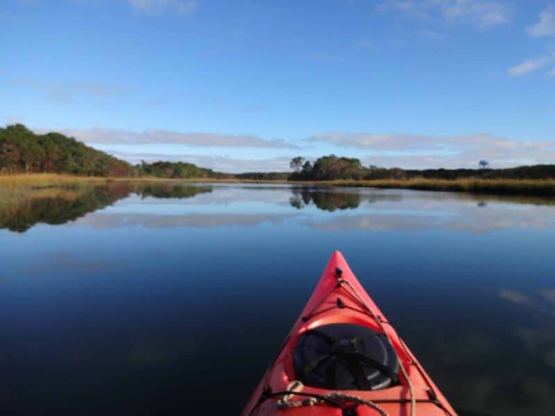 the front of a red kayak heading down a river