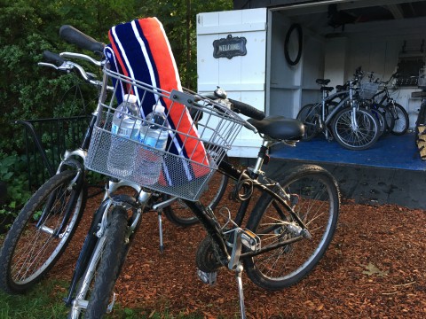 a photo of two bicycles with baskets that contain water bottles. they are in front of a shed full of bicycles
