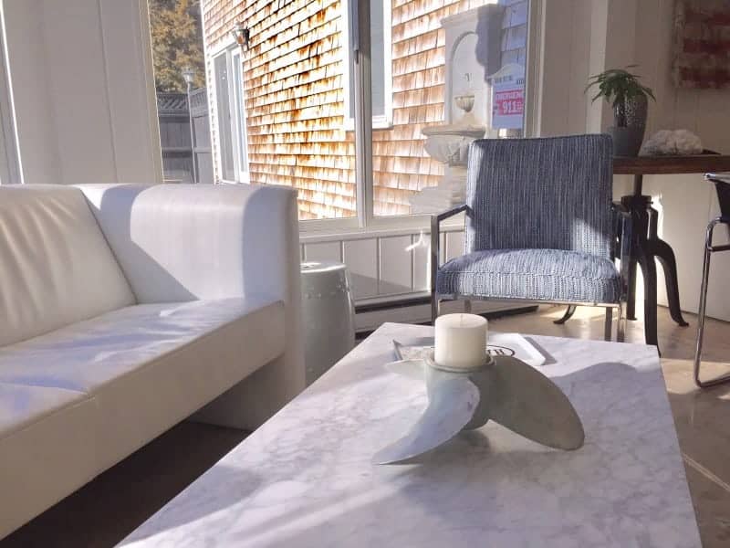 A sun filled room with a white leather couch and light blue chair.  A white coffee table has a propeller shaped candle holder on it