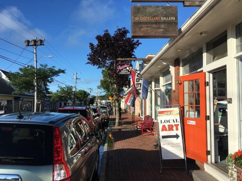 A small town street lined with cars and a variety of stores