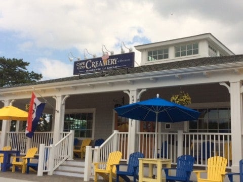 Exterior photo of Cape Cod Creamery with blue and yellow chairs and umbrellas out front