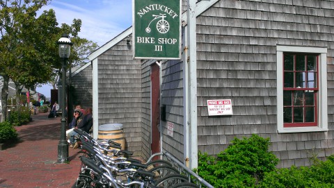 The shingled building of the Nantucket Bike Shop, with a green sign and bicycles parked in front