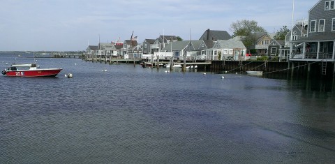 Nantucket harbor lined with small shacks on the shore, and a small red boat in the water.