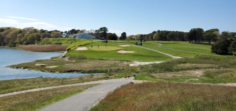 An asphalt golf cart path leads up to a putting green with sand traps around it