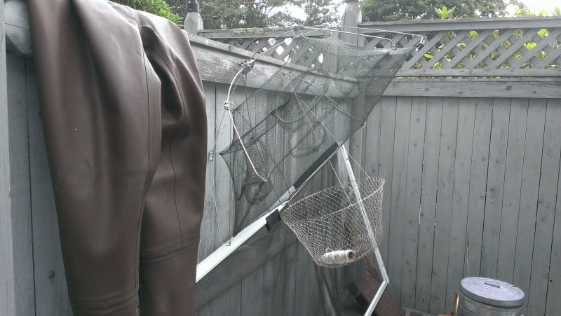 waterproof waders and a net and basket hang on a fence