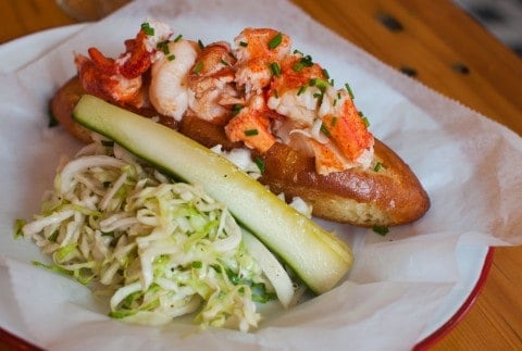 photo of a lobster roll with cole slaw and a pickle