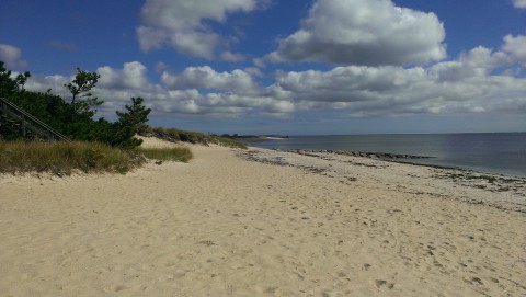 an empty beach and calm ocean with white clouds overhead