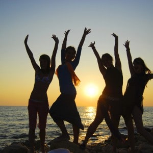 silhouette of four girls with raised hands on a beach at sunset