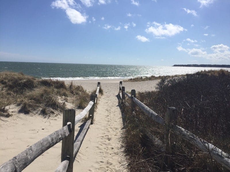 a split rail fence leads down a sandy path way to the ocean