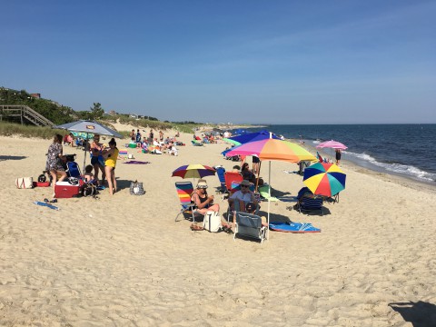 People gathering on the beach with umbrellas, towels and chairs