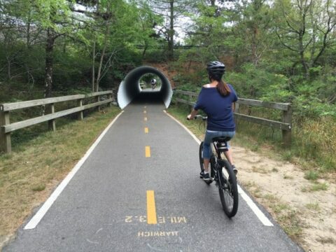 a girl on a bike driving towards a round metal tunnel on the bike path