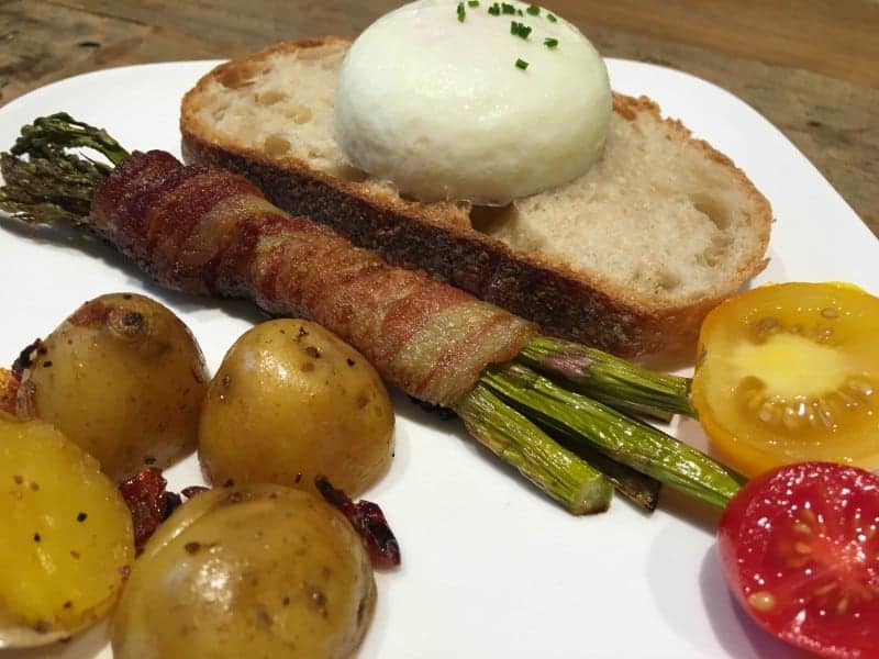 Photo of a breakfast plate with poached egg on toast, asparagus wrapped bacon and roasted potatoes and tomatoes