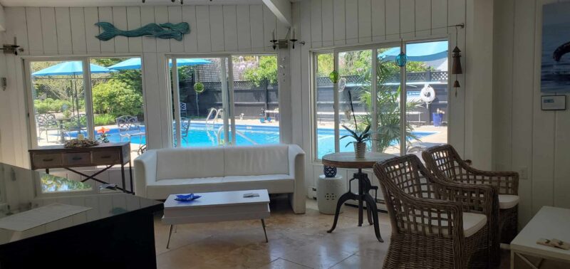 Room with white couches and woven chairs looking out to a pool