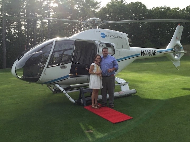 Helicopter on grass with a man and women standing in front of the helicopter