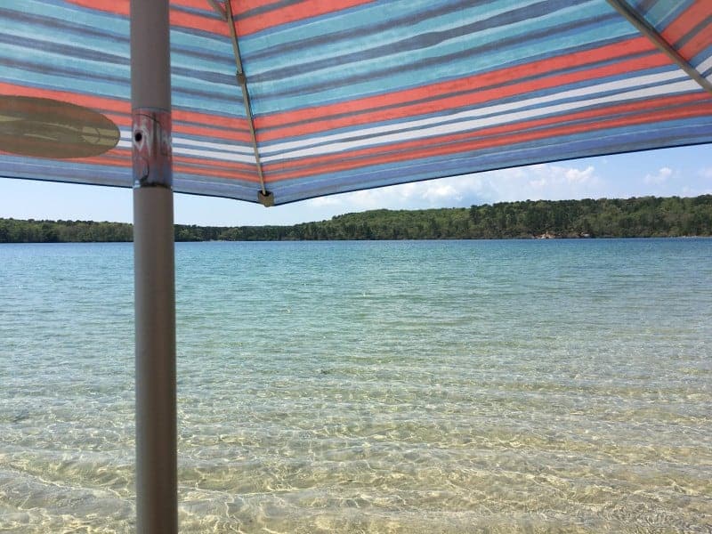 a multi color striped beach umbrella sticking out of the water of a pond