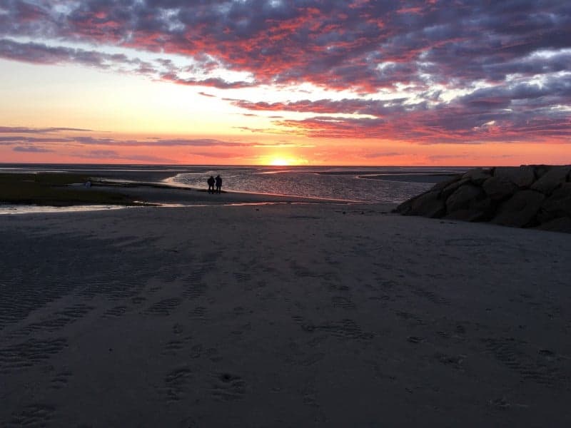 a couple walks the beach during a beautiful sunset