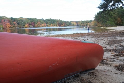 A red kayak sits on the shore of a kettle pond