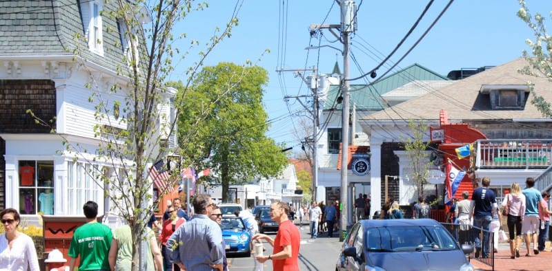 A photo of downtown Provincetown crowded with people and cars on a busy street with many shops
