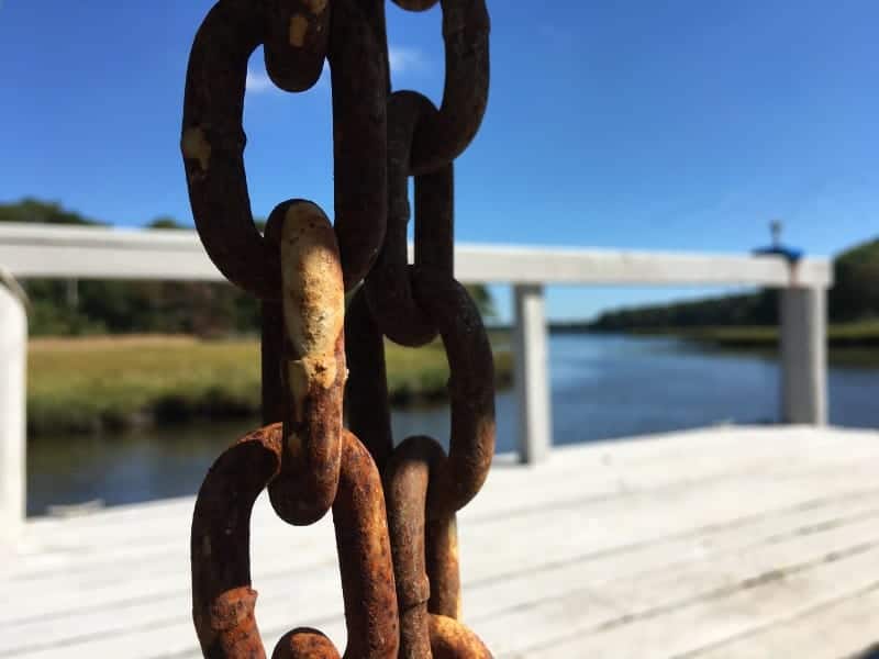 A rusted heavy chain in the foreground.  A dock beside a salt water estuary