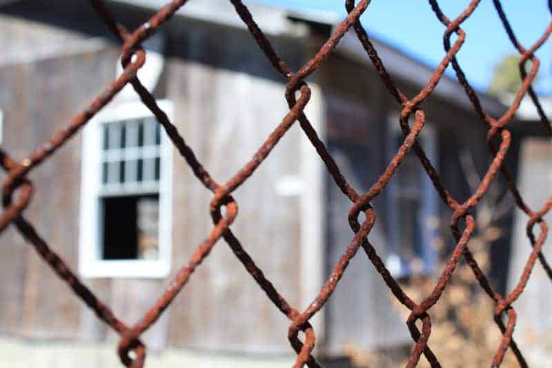 A building out of focus and seen through a rusty chain link fence