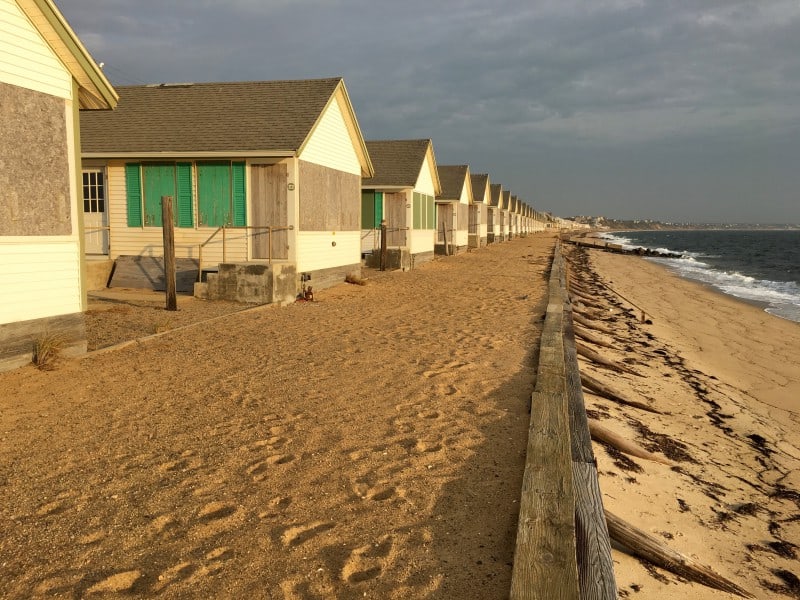 Dozens of small boarded up cottages, some with green shutters, by the ocean