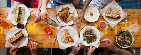 a table covered with food and drink and the hands of people reaching for them