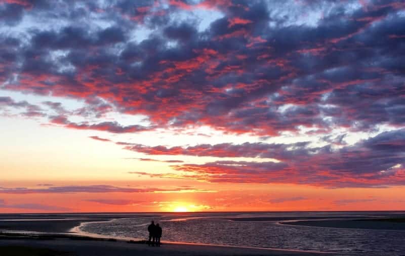 A couple walking along the beach and an amazing sunset with blue, red and orange clouds