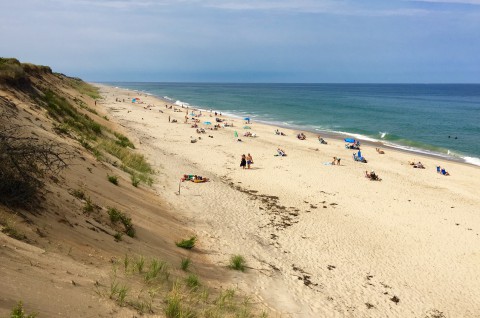 a sandy beach by the dunes and ocean with many people relaxing and walking