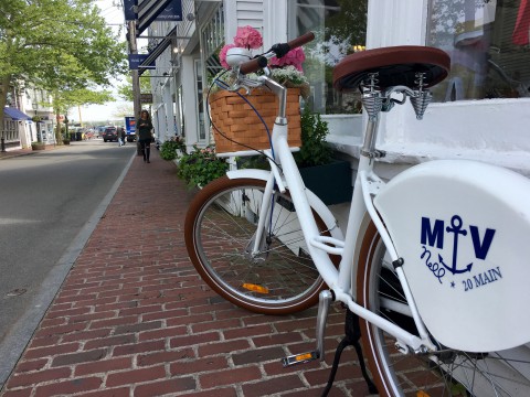 A brick walkway along a street in Martha's Vineyard.  A white bicycle with a woven basket is in the foreground