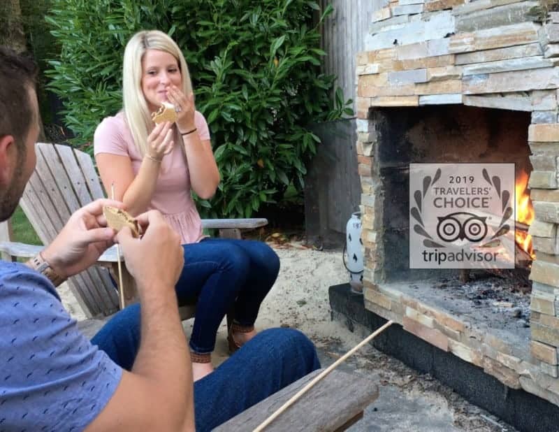 A couple enjoying eating s'mores by a stone outdoor fireplace