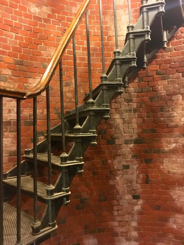 Curved metal stairs attached to a red brick wall inside of a lighthouse