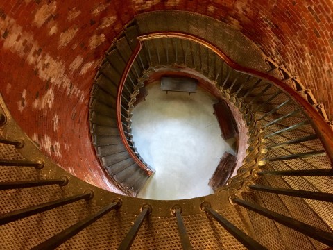 the inside of a light house showing the curve metal stairs and circular red bricked walls