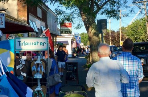 People walking down the side walk by store fronts with their wares displayed outside