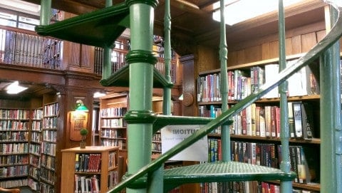 inside a bookstore with shelves of books and a green spiral staircase