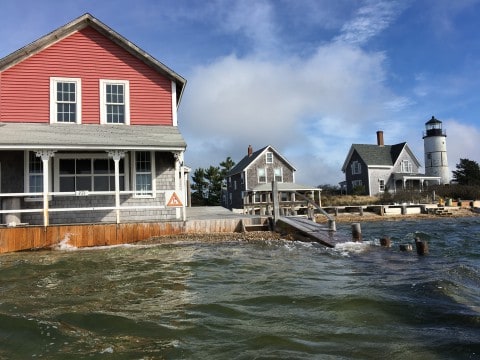 a red building sitting right on the water near another house and a light house