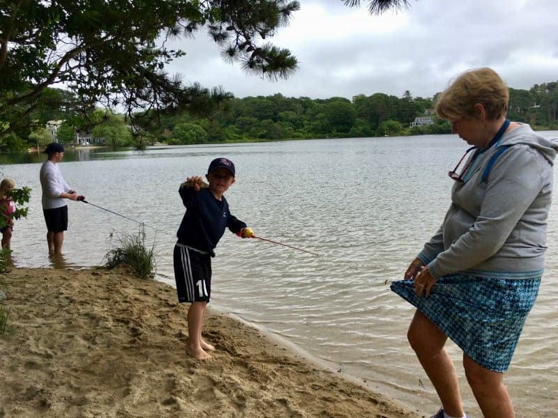 A man, woman and 2 children are fishing on a sandy shore by the ocean