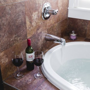 A tub being filled with water. A bottle of wine and 2 glasses.