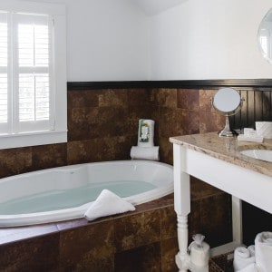 A white tub full of water surround by brown tile. A sink with bath amenities.