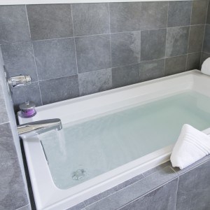 A soaking bathtub full of water and surrounded by grey tile