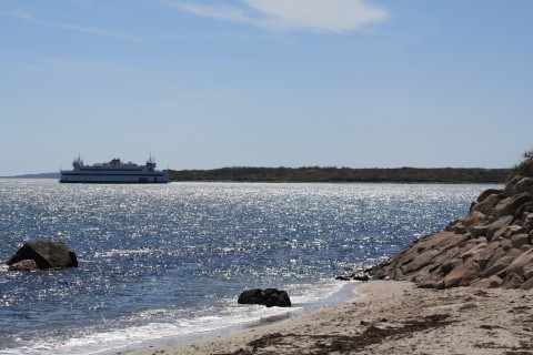 A sandy beach with a few rocks in the ocean, a ferry is in the distance