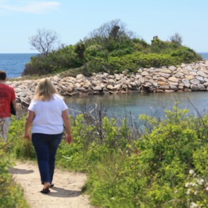 A woman with a white top is walking by a pond that is surrounded by rocks