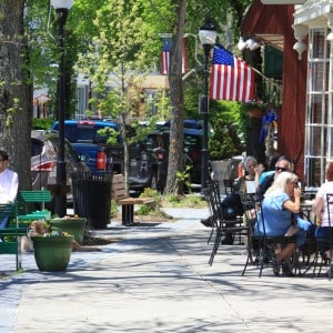 People sitting outside a restaurant on the sidewalk. An American flag is flying