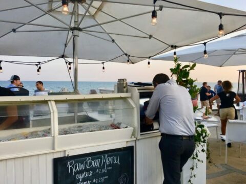 outdoor restaurant and raw bar by the ocean with a white umbrella over it covered in lights