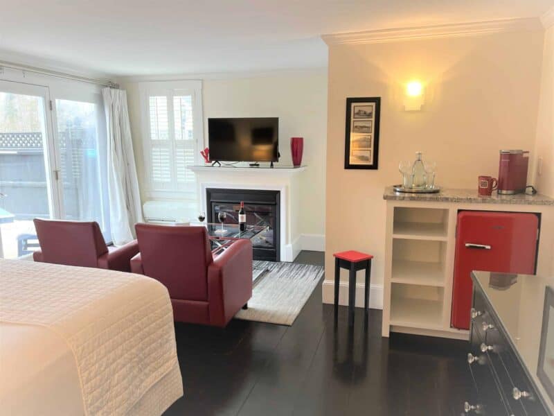 Bedroom decorated with red accents, features a gas fireplace with a tv above, a dry bar with red mini fridge