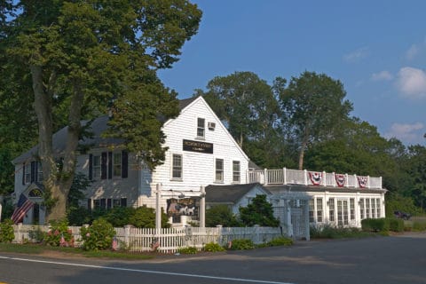 The exterior of the Old Yarmouth Inn, a white clapboard building surrounded by a white picket fence and trees