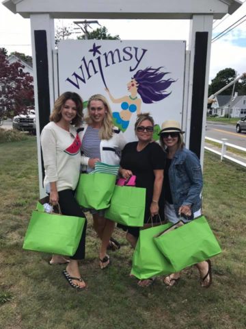 A group of women all holding lime green shopping bags in front of the Whimsy store sign